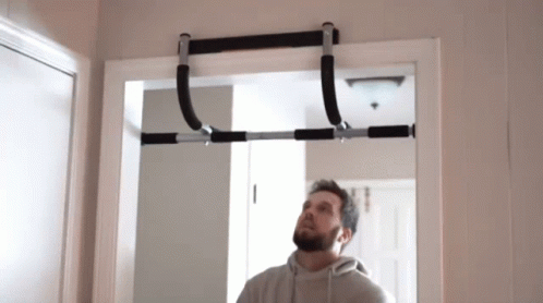 A Man Is Looking Up At A Pull Up Bar Hanging From A Doorway . GIF