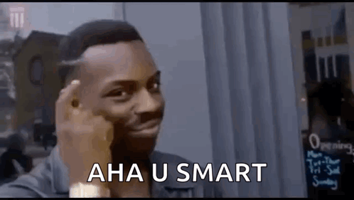 a man is making a funny face while holding his finger to his forehead and says `` aha u smart '' .