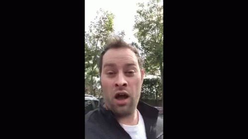 A Man Is Making A Funny Face While Wearing A Black Jacket And A White Shirt . GIF