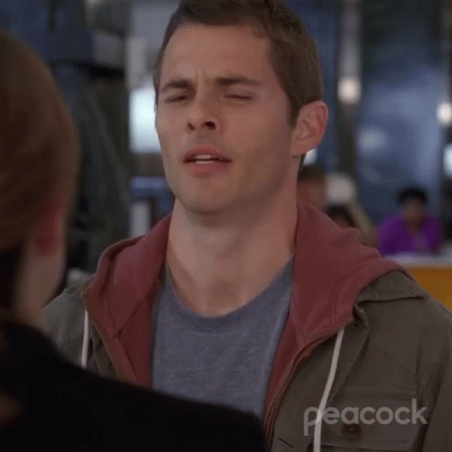 A Man Is Making A Funny Face With His Eyes Closed While Talking To A Woman . GIF
