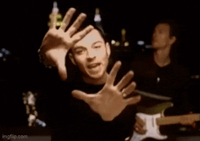 A Man Is Making A Funny Face With His Hands While Playing A Guitar In A Band . GIF