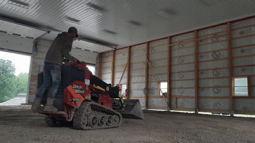 A Man Is Operating A Ditch Witch Tractor In A Garage GIF
