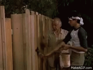A Man Is Painting A Wooden Fence With A Brush . GIF