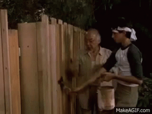 A Man Is Painting A Wooden Fence With A Brush . GIF