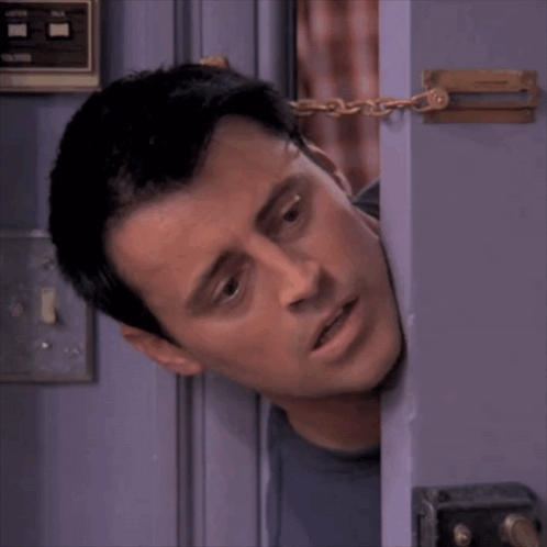 A Man Is Peeking Out From Behind A Door With A Chain Around His Neck GIF