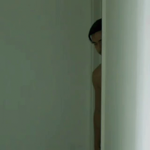 a man is peeking out of a doorway in a dark room .