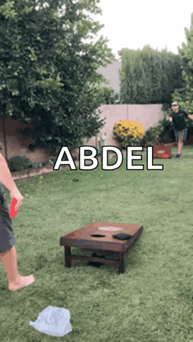 A Man Is Playing A Game Of Cornhole In A Backyard With The Name Abdel On The Bottom GIF