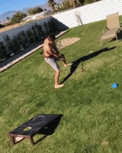 A Man Is Playing A Game Of Cornhole In The Backyard GIF