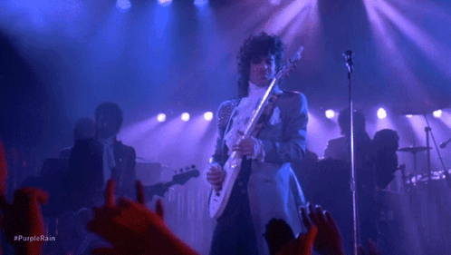 A Man Is Playing A Guitar And Singing Into A Microphone On A Stage . GIF