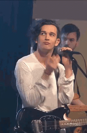 A Man Is Playing A Guitar And Singing Into A Microphone . GIF