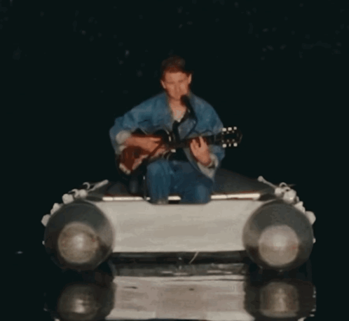 A Man Is Playing A Guitar And Singing Into A Microphone GIF