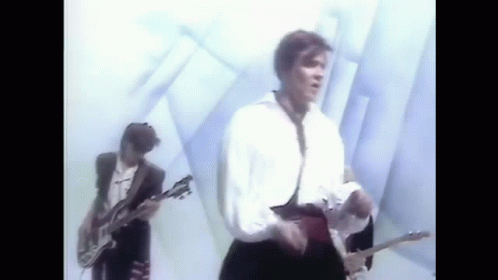 A Man Is Playing A Guitar In A Band While Another Man Sings . GIF