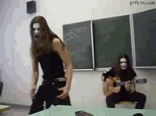 A Man Is Playing A Guitar In A Classroom And A Woman Is Dancing . GIF