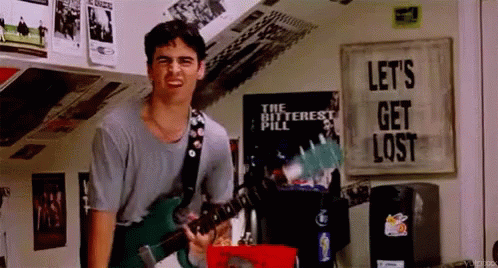 A Man Is Playing A Guitar In A Room With A Sign That Says Let 'S Get Lost GIF