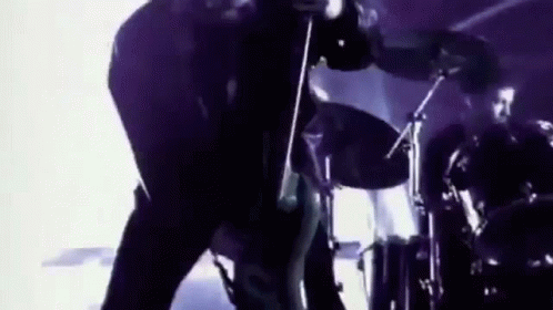 A Man Is Playing A Guitar In Front Of A Drum Set . GIF