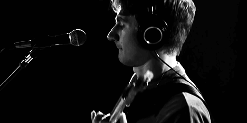 A Man Is Playing A Guitar In Front Of A Microphone In A Black And White Photo GIF