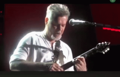 A Man Is Playing A Guitar In Front Of A Microphone GIF