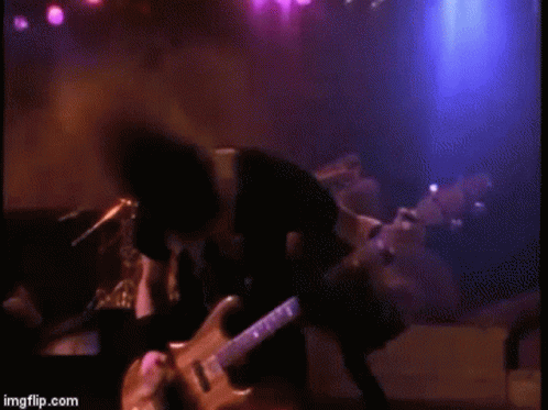 A Man Is Playing A Guitar On A Stage In A Dark Room . GIF