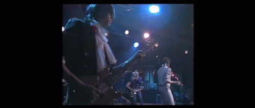 A Man Is Playing A Guitar On A Stage While Another Man Sings Into A Microphone . GIF