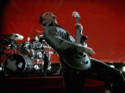 A Man Is Playing A Guitar On A Stage With A Drummer In The Background . GIF