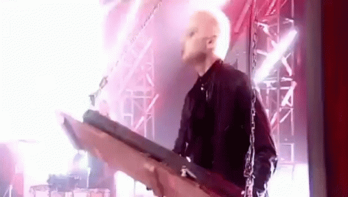 A Man Is Playing A Guitar On A Stage With Chains Around Him . GIF