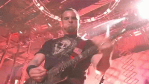 A Man Is Playing A Guitar On Stage In A Dark Room . GIF