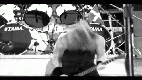 A Man Is Playing A Guitar On Stage In Front Of A Drum Set . GIF