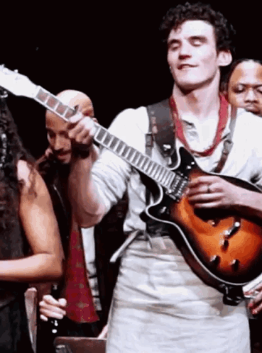 A Man Is Playing A Guitar On Stage In Front Of A Group Of People GIF