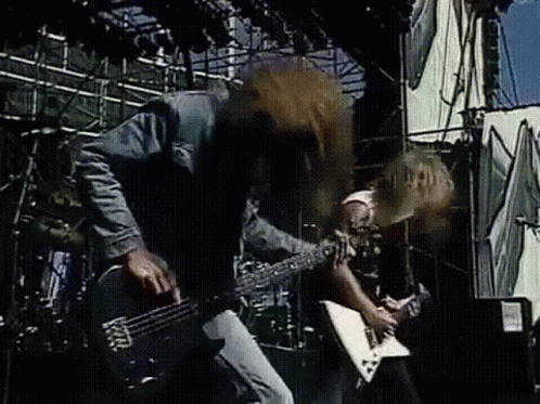 A Man Is Playing A Guitar On Stage While Another Man Drums . GIF