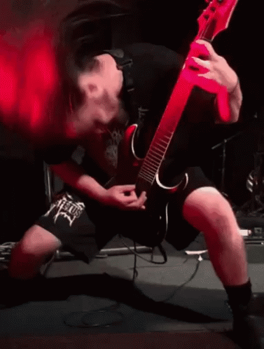 A Man Is Playing A Guitar On Stage With Red Smoke Coming Out Of His Mouth . GIF