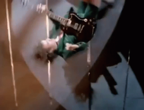 A Man Is Playing A Guitar Upside Down On A Skateboard . GIF