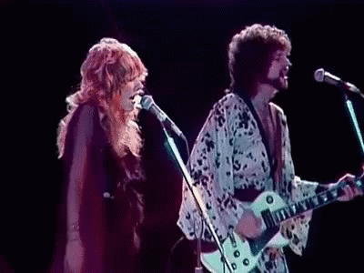 A Man Is Playing A Guitar While A Woman Sings Into A Microphone On Stage . GIF
