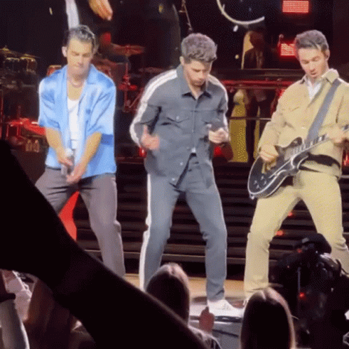 A Man Is Playing A Guitar While Another Man Is Singing On Stage GIF