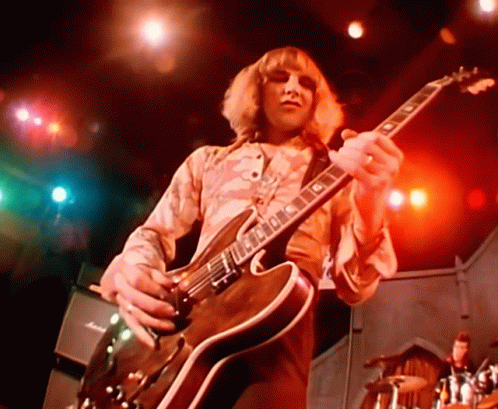 A Man Is Playing A Guitar With The Letter G On The Neck GIF