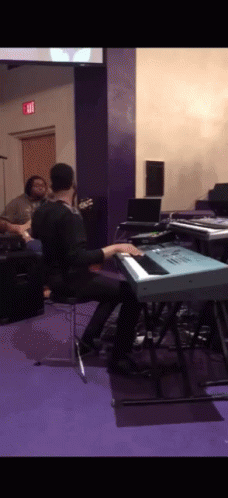 A Man Is Playing A Keyboard In A Room With An Exit Sign On The Wall GIF