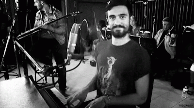 A Man Is Playing A Piano In A Black And White Photo While A Band Plays In The Background . GIF
