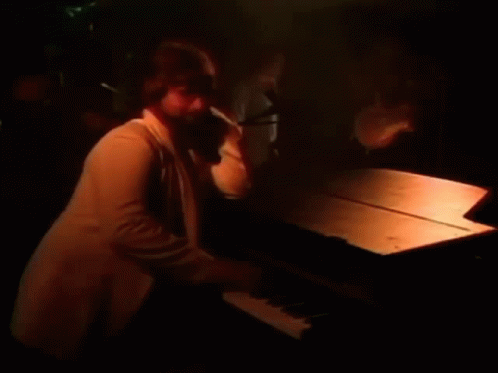 a man is playing a piano in a dark room with a microphone in the background .