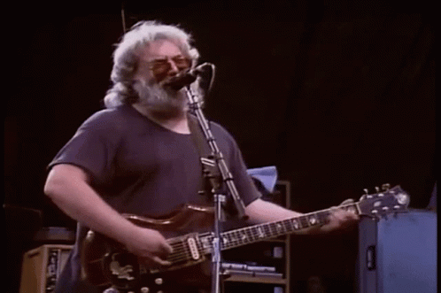 A Man Is Playing A Piano On A Stage While A Band Plays Behind Him . GIF