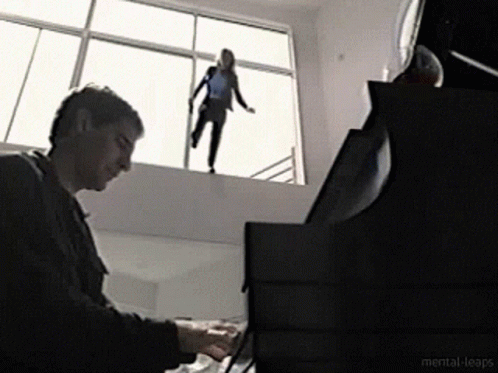 A Man Is Playing A Piano While A Woman Is Standing On A Window Sill GIF