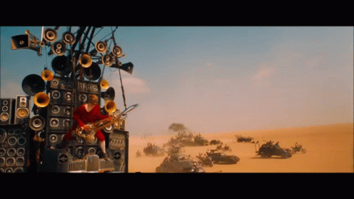 A Man Is Playing A Saxophone In Front Of A Wall Of Speakers In The Desert GIF