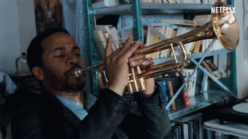 A Man Is Playing A Trumpet In Front Of A Shelf With Netflix Written On The Bottom GIF