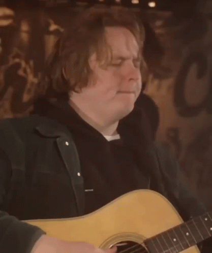 A Man Is Playing An Acoustic Guitar In Front Of A Sign That Says C GIF