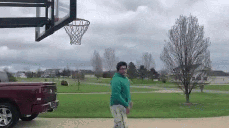 A Man Is Playing Basketball In Front Of A Basketball Hoop In A Park . GIF