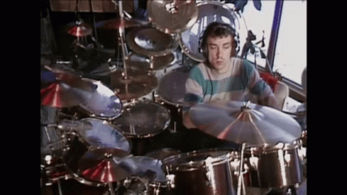 A Man Is Playing Drums In A Room With A Lot Of Drums And Cymbals . GIF