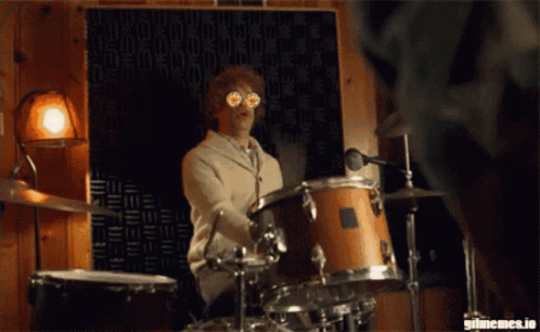 A Man Is Playing Drums In Front Of A Wall That Says Gifmemes.io On It GIF
