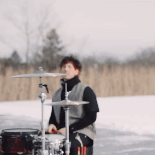 A Man Is Playing Drums In The Snow In A Field GIF