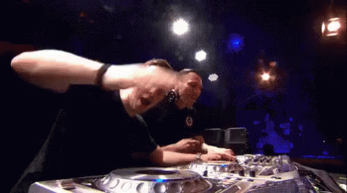 A Man Is Playing Music On A Mixer In A Dark Room . GIF