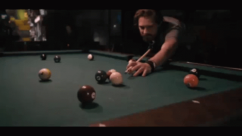 A Man Is Playing Pool With A Cue And Balls That Have The Number 8 On Them GIF