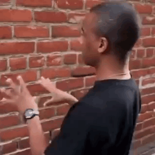A Man Is Pointing At A Brick Wall While Wearing A Watch . GIF