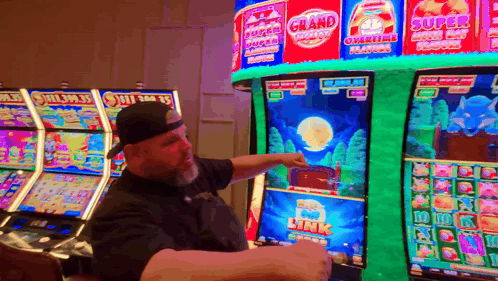 A Man Is Pointing At A Slot Machine That Has The Word Grand On It GIF